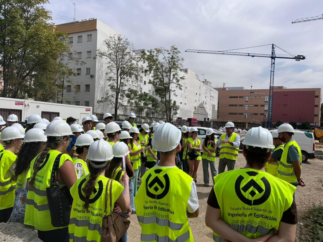 Fotografía del alumnado en obra, vistinedo chaleco y casco de seguridad. De fonde se aprecia una grúa.