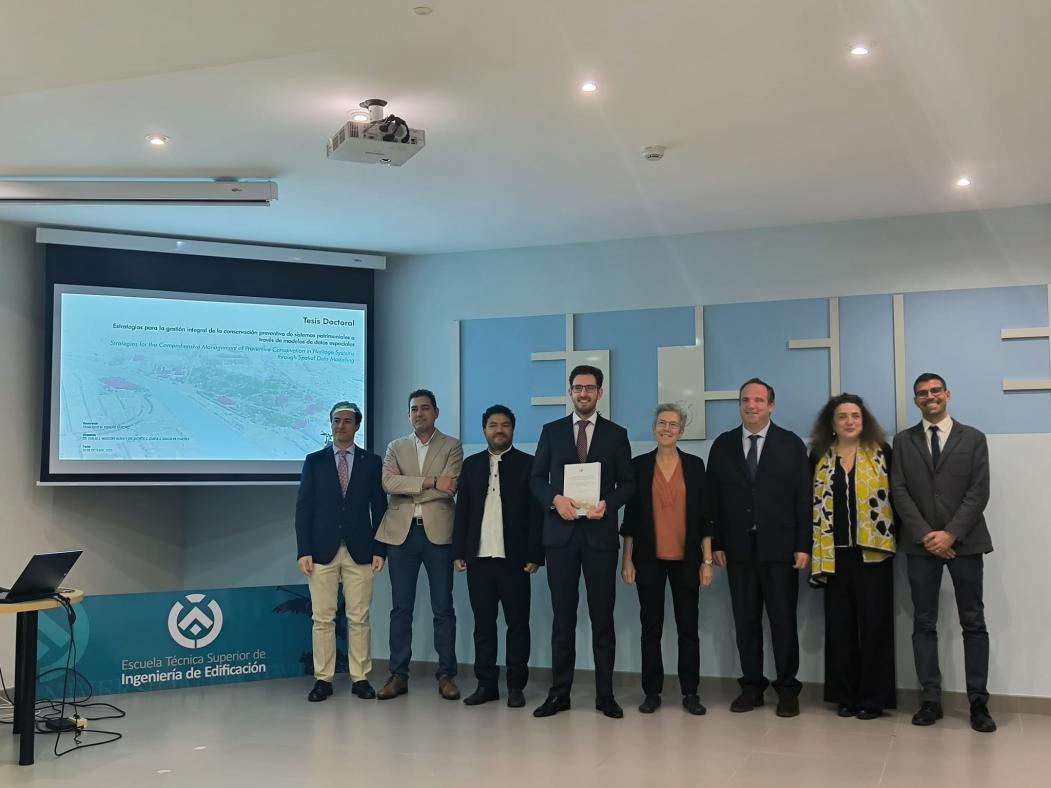 Fotografía de Francisco Hidalgo junto al tribunal y Directores de Tesis, junto a la pantalla de exposición en el salón de Grados.
