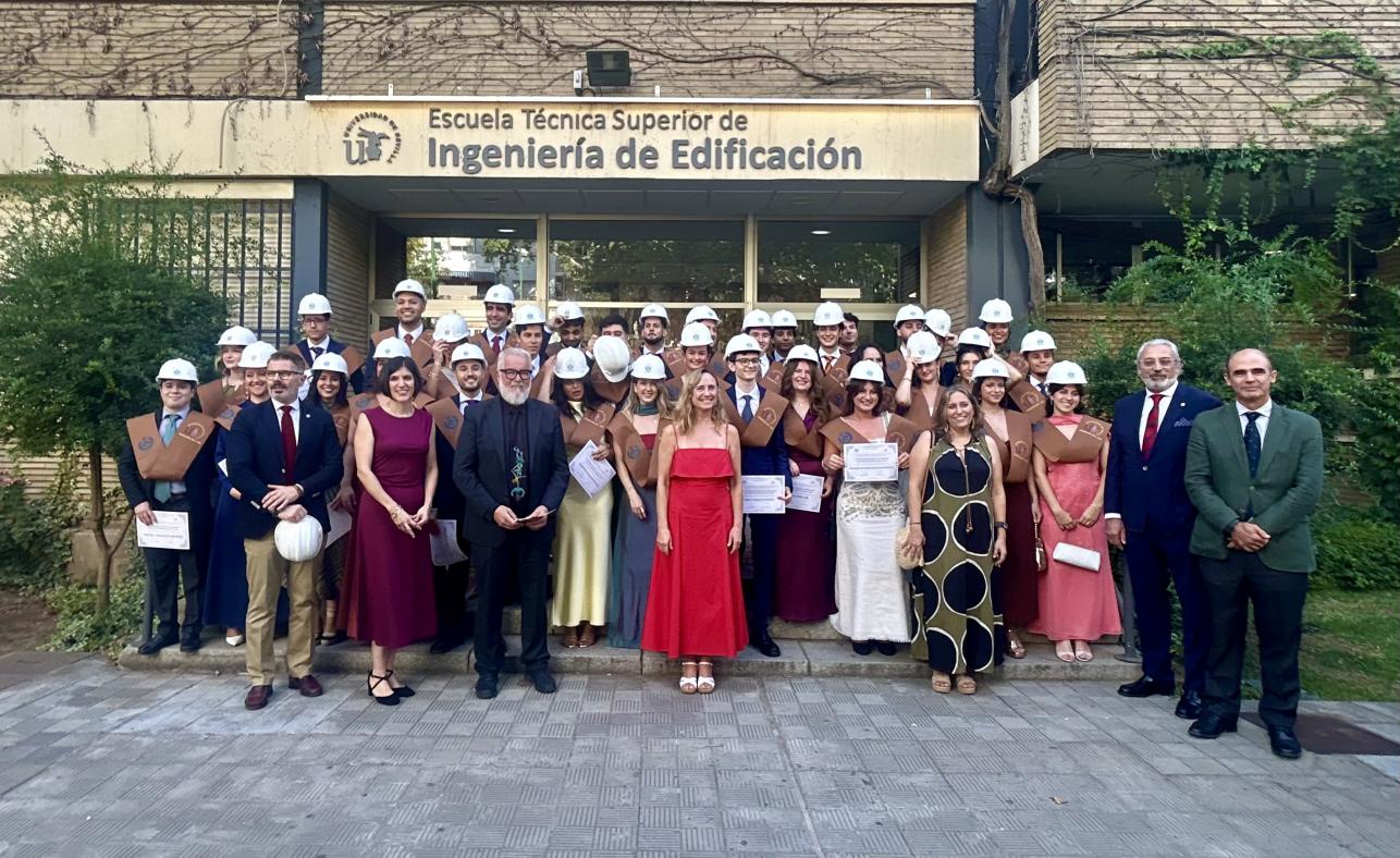 Fotografía del alumnado graduado y el profesorado asistente al acto, delante de la entrada a la ETSIE, bajo el letrero de Escuela Técnica Superior de Ingeniería de Edificación.