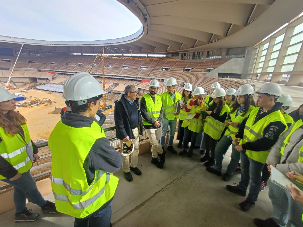 Fotografía del alumnado, con chalecos de seguridad y cascos de obra, visitando las instalaciones del estadio junto al jefe de obras.