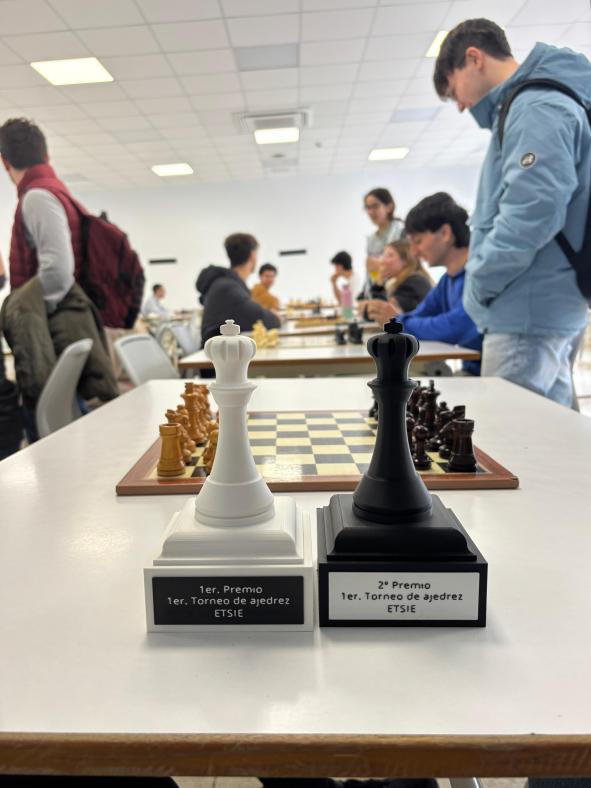 Imagen de los trofeos, de fondo un tablero de ajedrez y la silueta borrosa de estudiantes.
